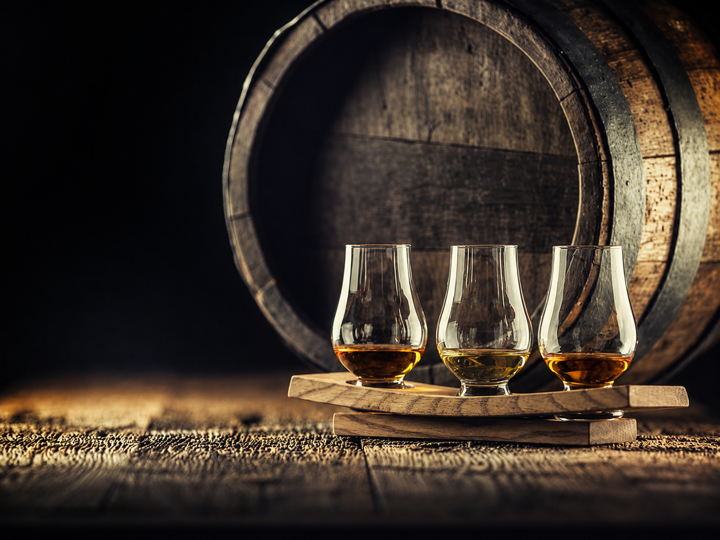 Three whisky samples presented for comparative tasting beside an oak cask