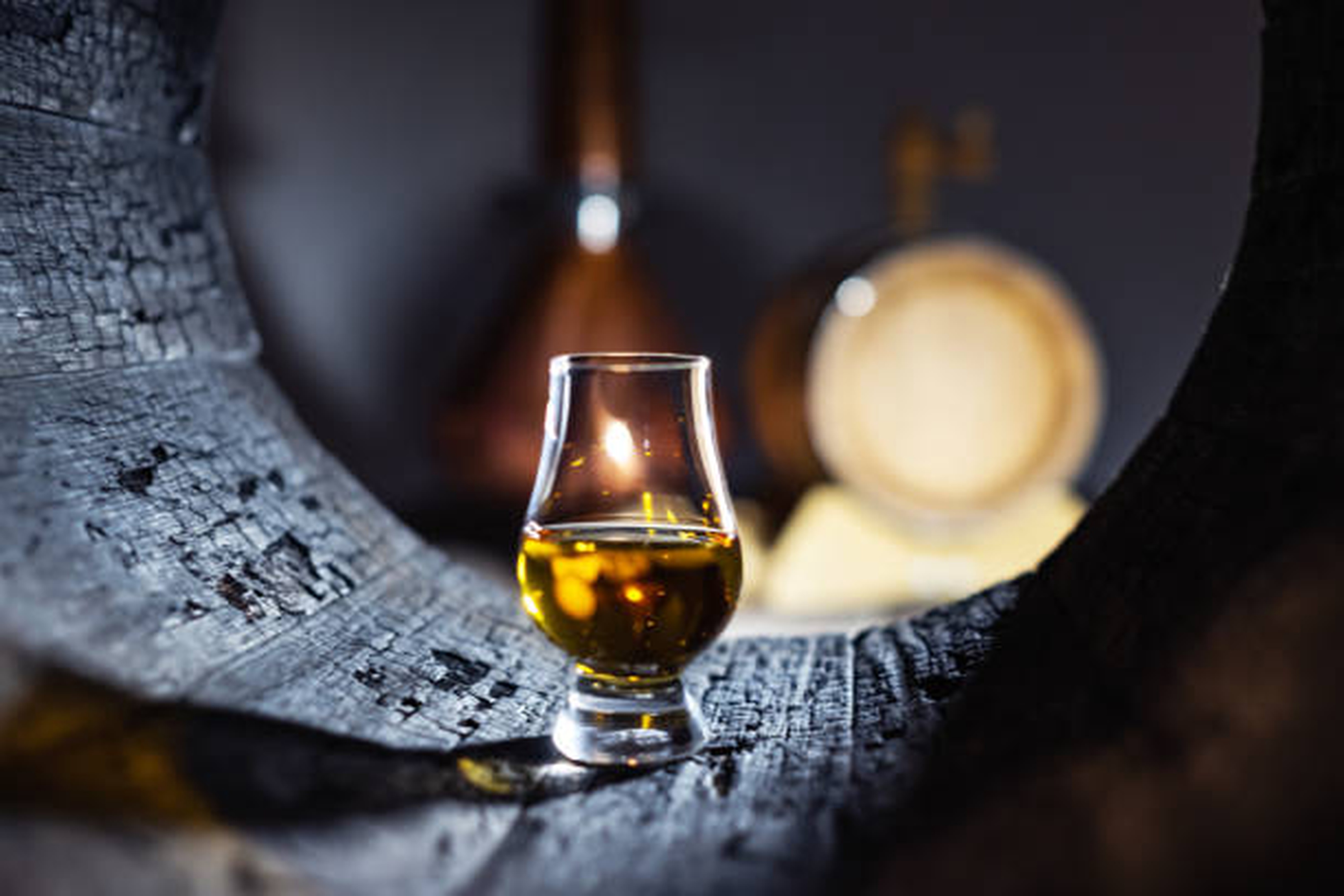 Glencairn glass of whiskey framed inside a charred barrel